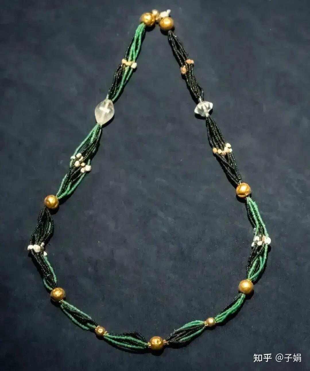 Green and black bead necklace with gold-colored accents on a dark background