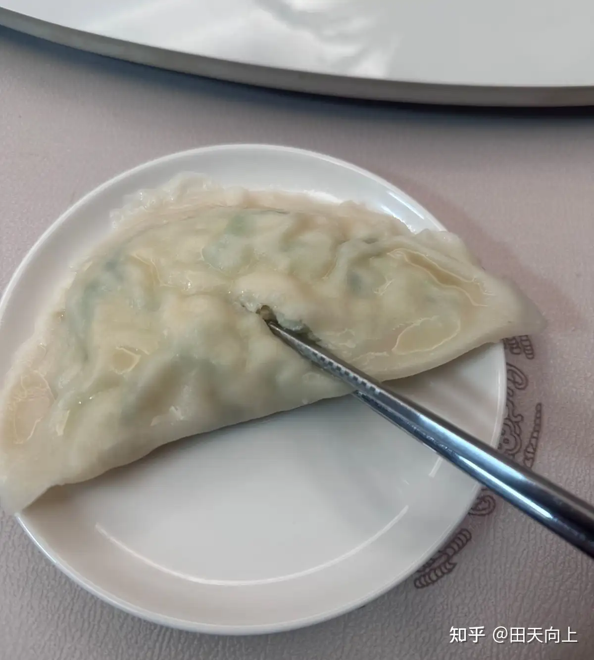 A plate of boiled dumplings with a spoon on a restaurant table