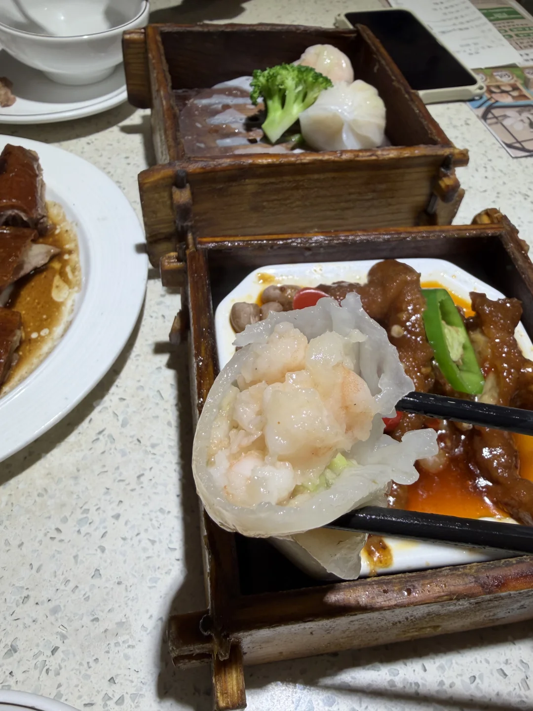 A shrimp dumpling held with chopsticks above bamboo-style dim sum steamers in Guangzhou