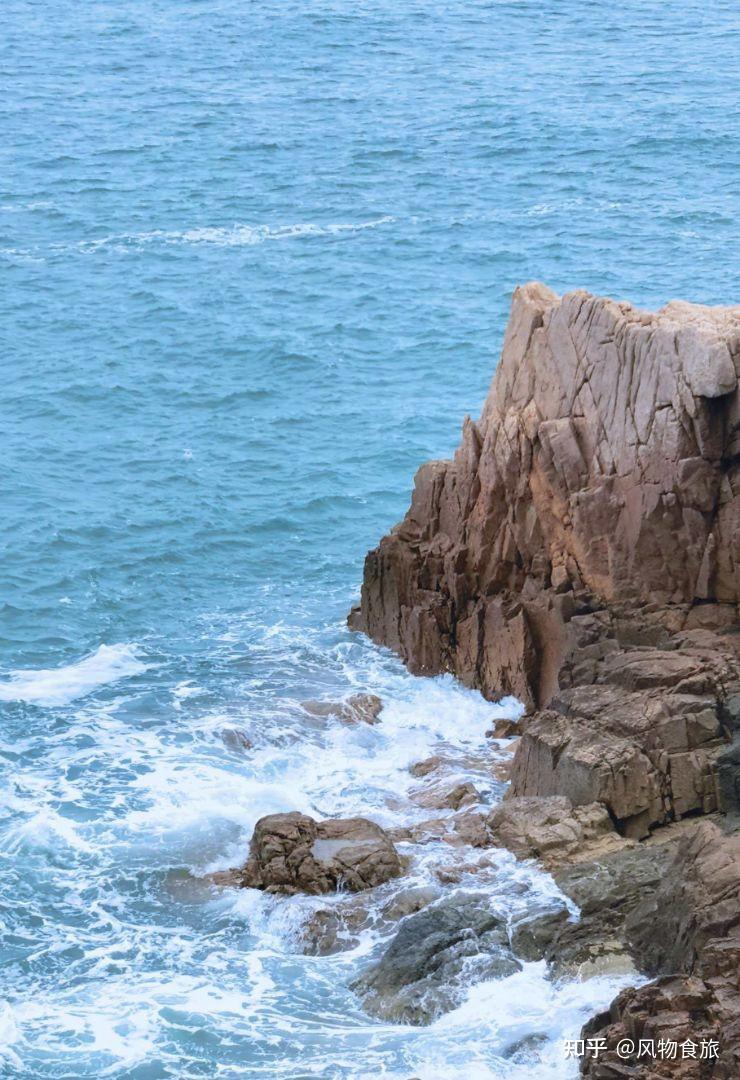 Blue sea breaking around a rocky Qingdao shoreline under clear light